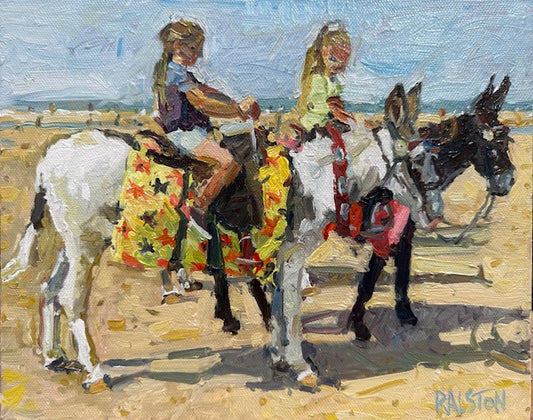 Two children riding donkeys on a beach with a colorful saddle blanket.