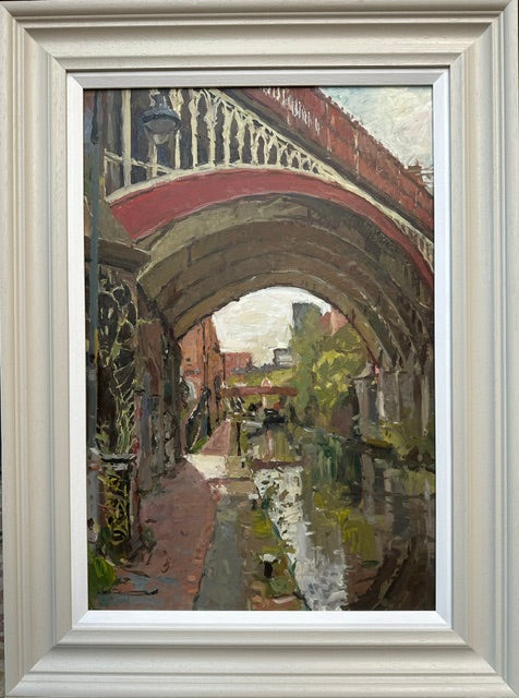A framed oil painting depicting a scenic Rochdale canal at Deansgate Manchester under a red arched bridge, with a light-colored wooden frame.