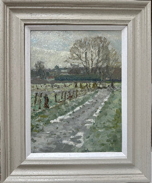 A framed landscape oil painting depicting a rural path leading through a grassy field toward leafless trees under a cloudy sky, housed in a wide, light gray wooden frame with a white mat.