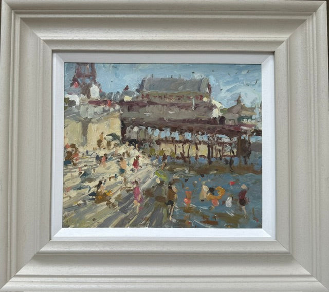 A framed impressionist painting of a seaside pier with people, housed in a wide, light-colored decorative frame with a white mat.