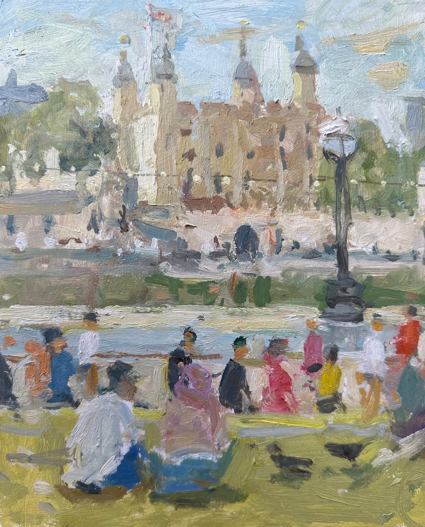 A view across the Thames towards the Tower of London, with people and pigeons on the grass at summertime