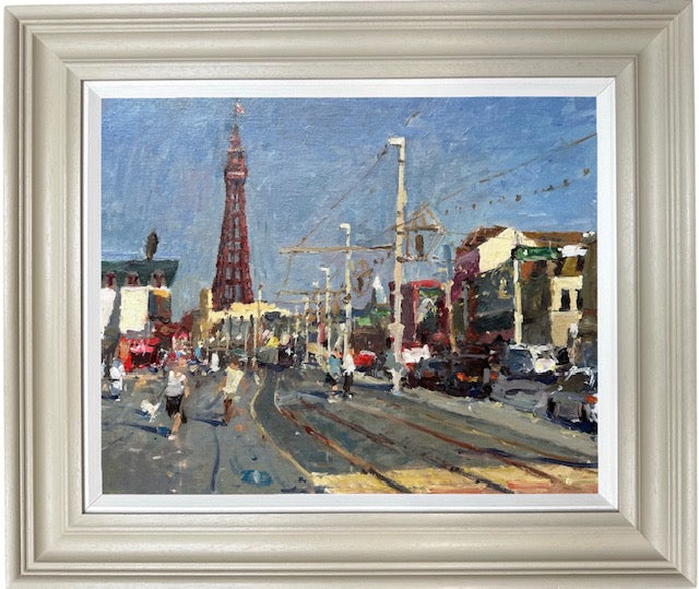 A framed impressionist plain air oil painting of a street scene featuring Blackpooltower, tram tracks, and buildings under a blue sky, housed in a light beige frame with a white mat. Painted by northern artist Adam Ralston
