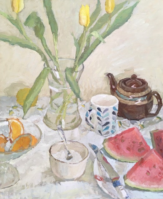 A still life painting of a tabletop scene with yellow tulips in a glass vase, a brown teapot, a patterned mug, watermelon slices, orange slices, and a small bowl with a spoon on a light tablecloth.