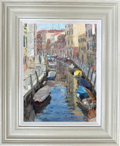 A framed impressionist oil painting of a Venetian canal with boats and buildings, presented in a wide, light-colored frame with a white mat.