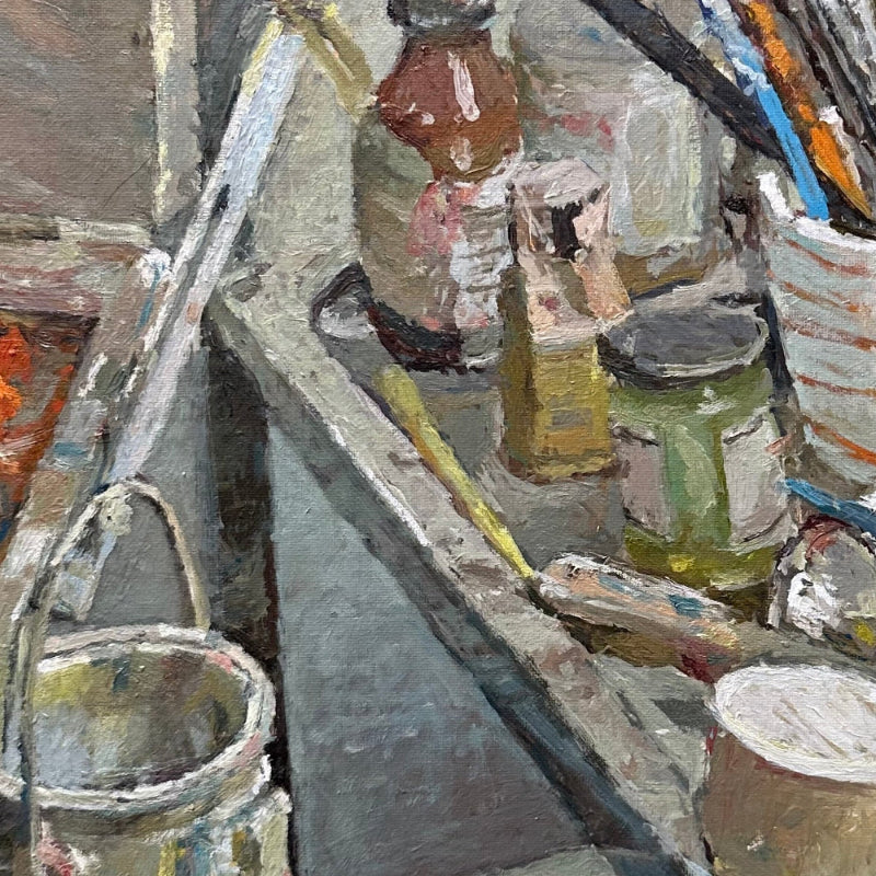 An impressionistic oil painting depicting an artist's studio clutter, featuring paint tubes, brushes, jars, and canvas rollers with visible thick brushstrokes.