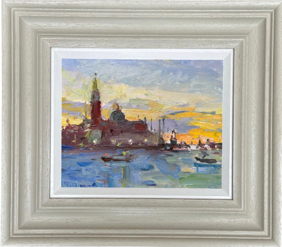 A framed impressionist-style painting of a waterfront city scene at Venice sunset, with blue water, red-brown buildings, and a yellow sky, set in a wide light gray frame.