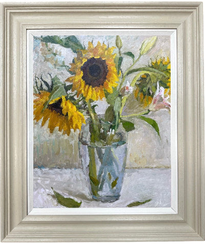 Framed still life painting of sunflowers in a glass vase, with a light wood frame and white matting.