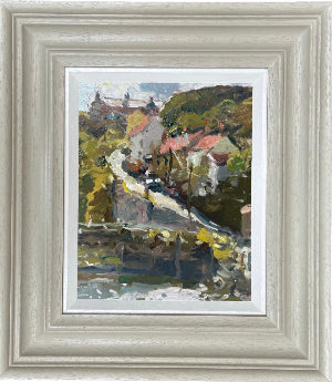 A framed landscape oil painting featuring a village scene in Staithes with white houses, red roofs, and green hills with centre jour light on the Beck.